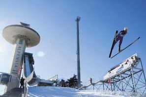 A ski jump ramp with a skier in mid-air, a tall observation tower, and a ski lift structure. - InterContinental ALPENSIA PYEONGCHANG RESORT by IHG (Pyeongchang-gun)