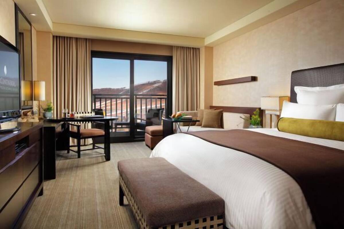 Ein Hotelzimmer mit einem großen Bett, einem Schreibtisch mit Stuhl, einem kleinen Tisch und Blick auf die Wüste durch das Fenster.