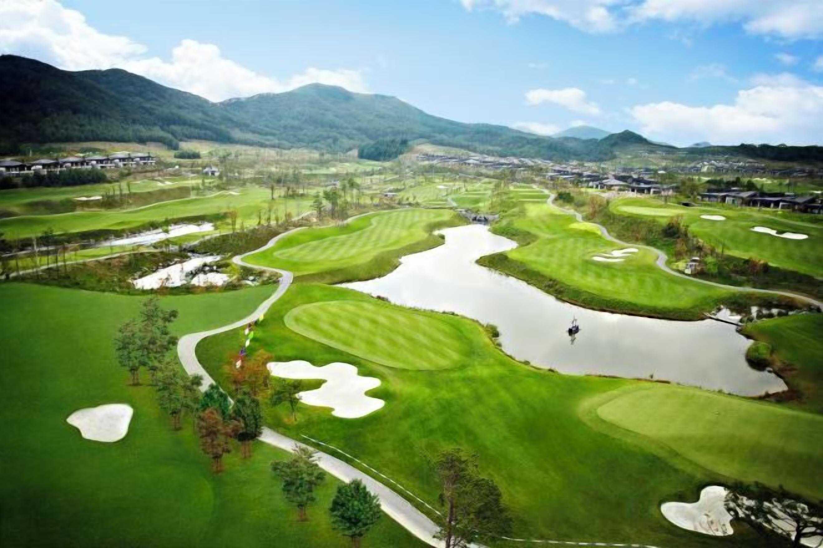 A golf course with multiple water hazards, a putting green, and a view of distant mountains.