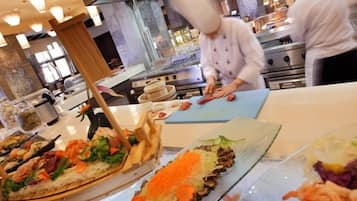 Un espace cuisine où des chefs préparent des plats, un buffet proposant divers mets et, au fond, un grand four.