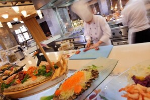 A kitchen area with chefs preparing food, a buffet with various dishes, and a large oven in the background. - InterContinental ALPENSIA PYEONGCHANG RESORT by IHG (Pyeongchang-gun)