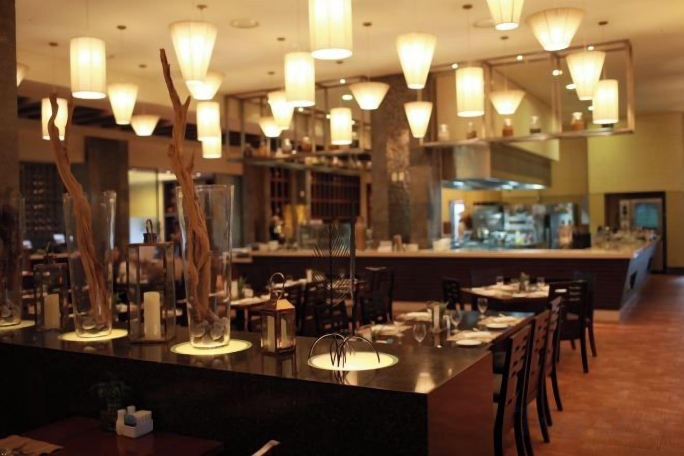 A restaurant interior with a bar area, dining tables, chairs, and pendant lighting.