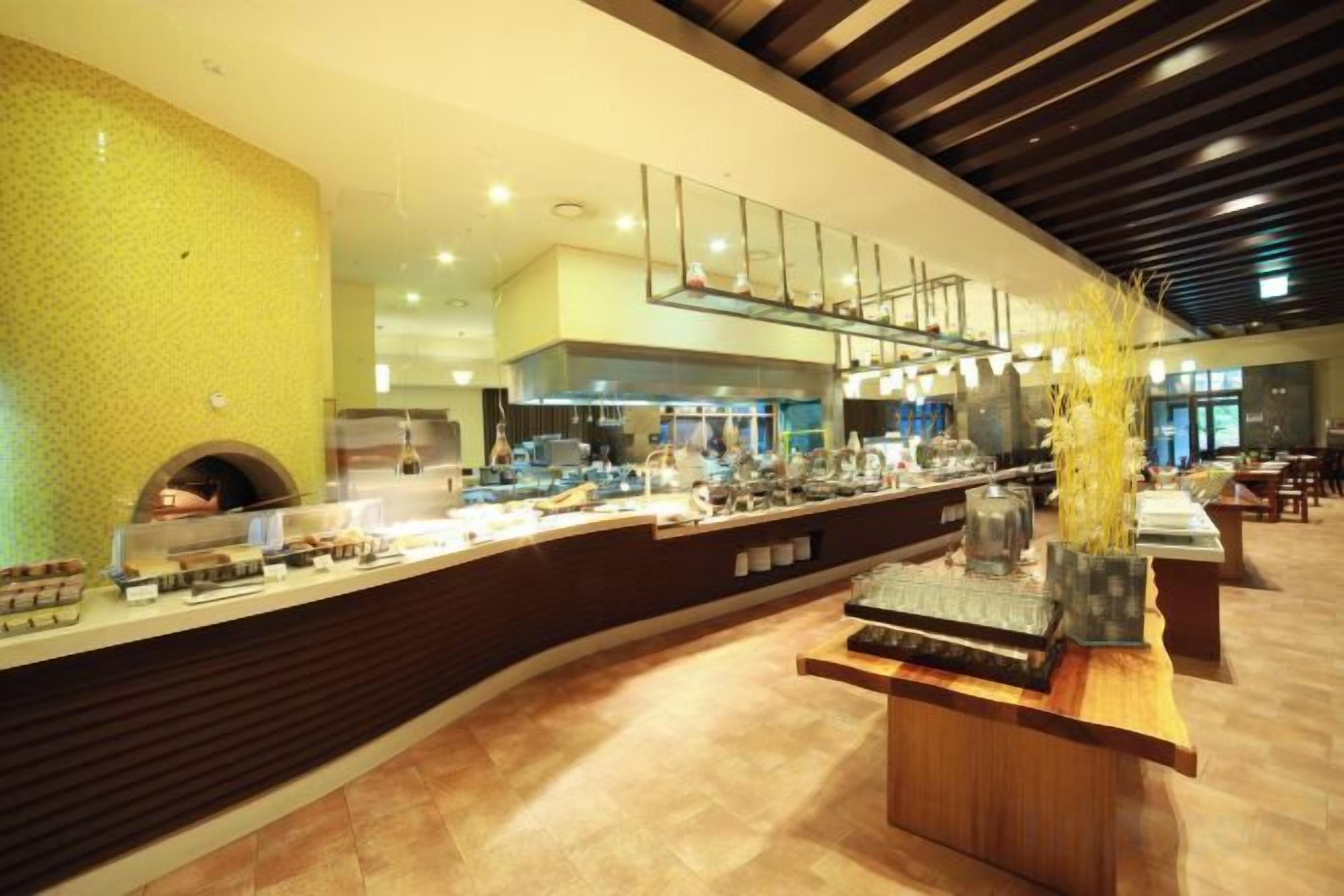 A modern hotel lobby with a curved reception desk, a large yellow textured wall, and a seating area with tables and chairs.