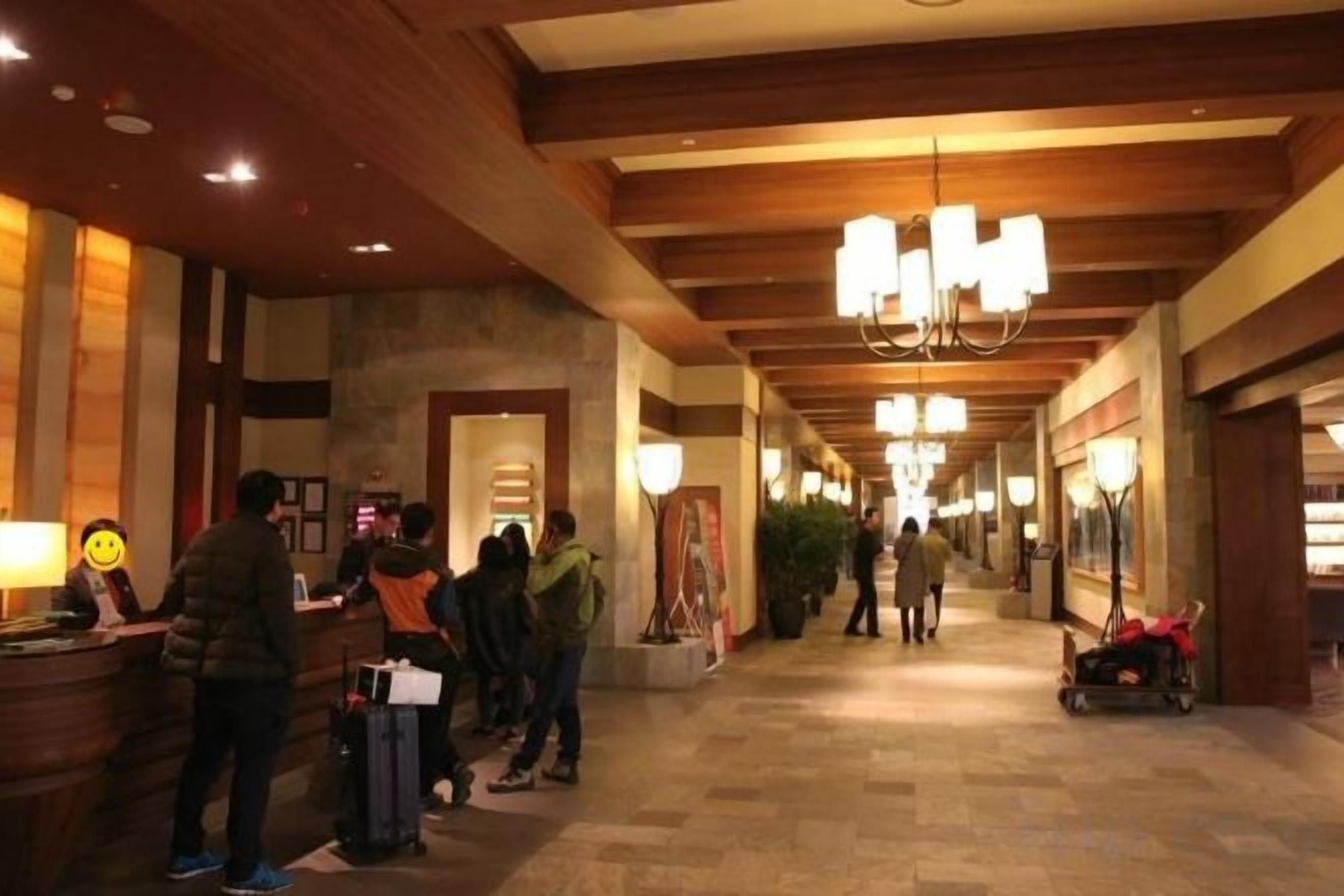 A hotel lobby with a reception desk, a chandelier, and a corridor with a tiled floor.