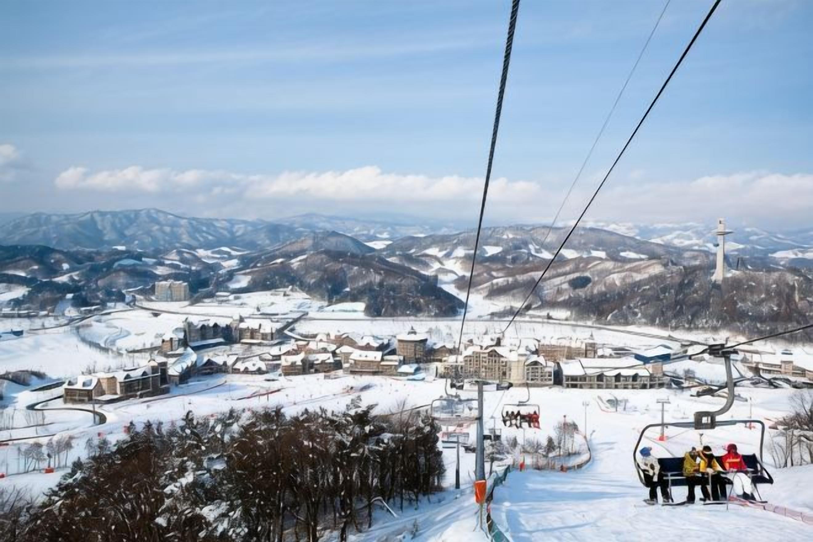 Eine Sesselbahn mit Blick auf eine verschneite Stadt und Berge im Hintergrund.
