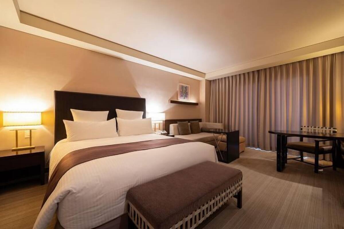 Ein Hotelzimmer mit einem großen Bett, Nachttischen, einem Schreibtisch und einem Esstisch.