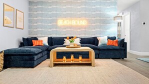 A living room with a dark blue sectional sofa, a wooden coffee table, and a neon sign on the wall. - Pickleball court, heated pool, mins to the beach, game room & tons of amenities. (Largo)