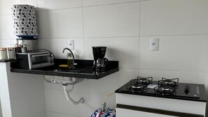 A compact kitchen with a gas stove, a toaster, and a coffee maker. - CASA DOS VENTOS (Praia Grande)