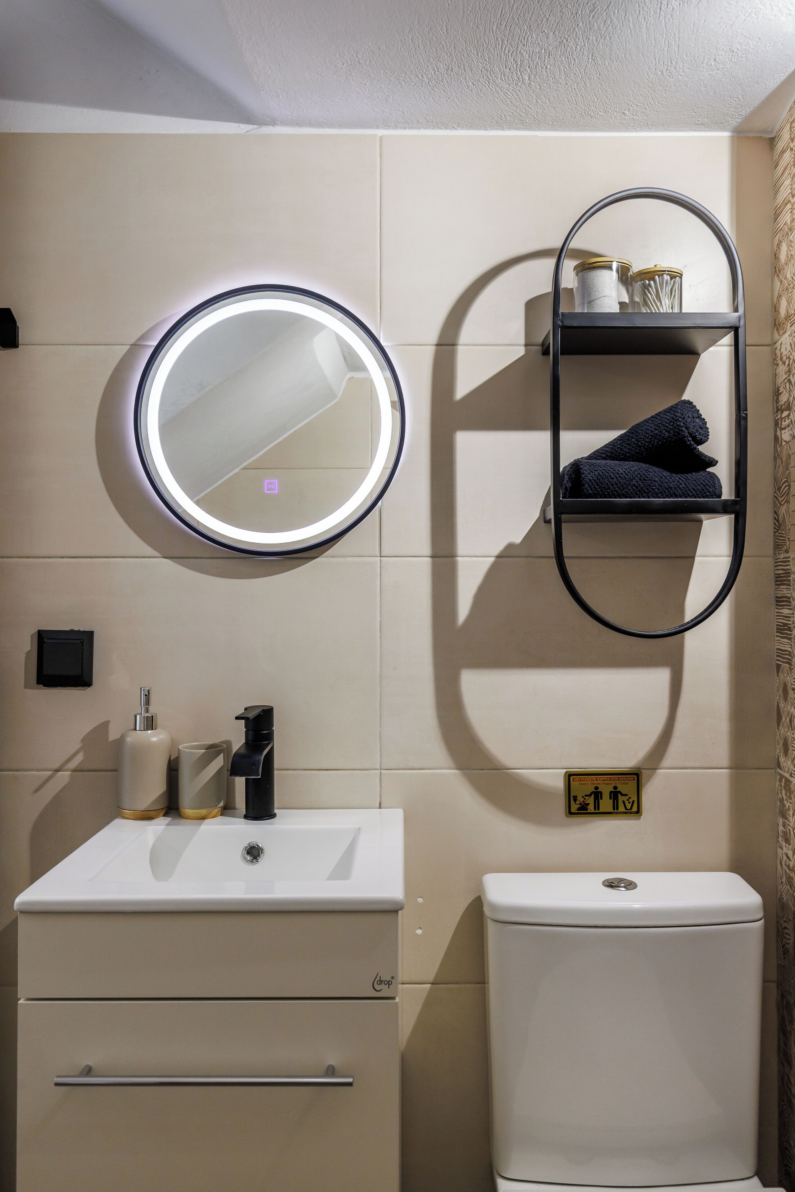 Un baño con un espejo redondo, un lavamanos, un inodoro y un perchero para toallas.