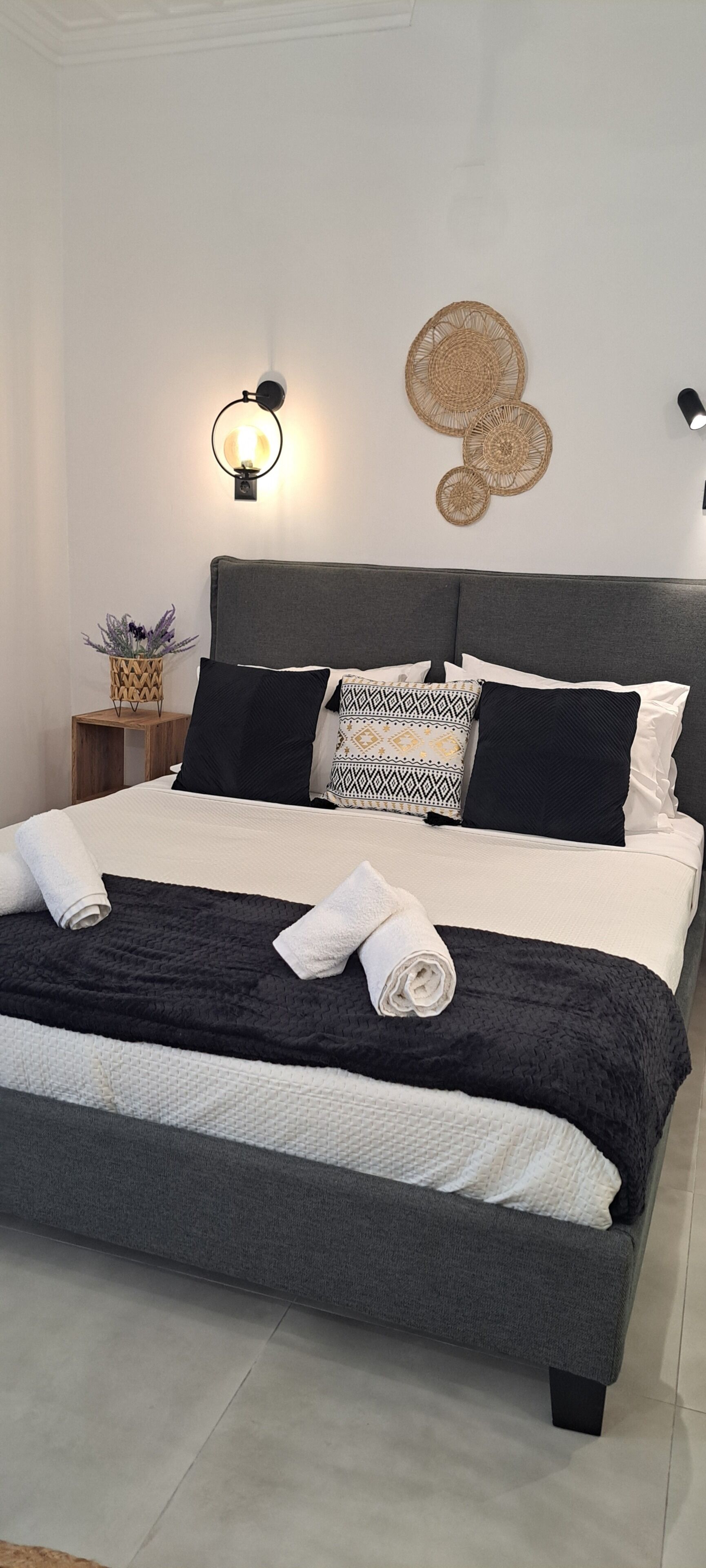 Una cama bien tendida con un cabecero gris, almohadas estampadas en blanco y negro y una manta negra.