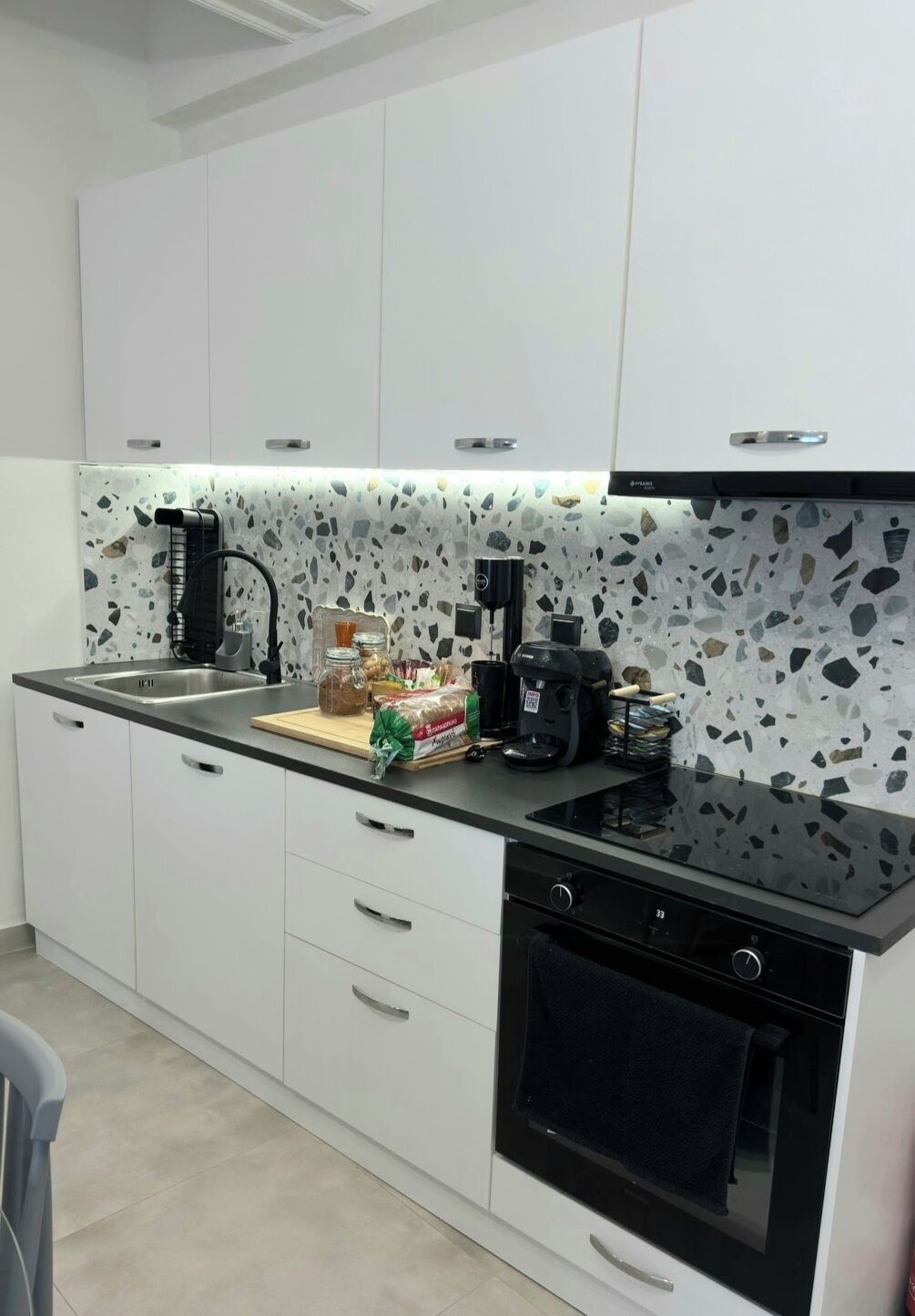 Eine moderne Küche mit weißen Schränken, einer schwarzen Arbeitsplatte, einer Kaffeemaschine und einem Toaster.