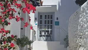 Un escalier étroit en pierre mène à un bâtiment blanc doté d’une grille en métal, qui est entouré de plantes en pot et d’un arbre.