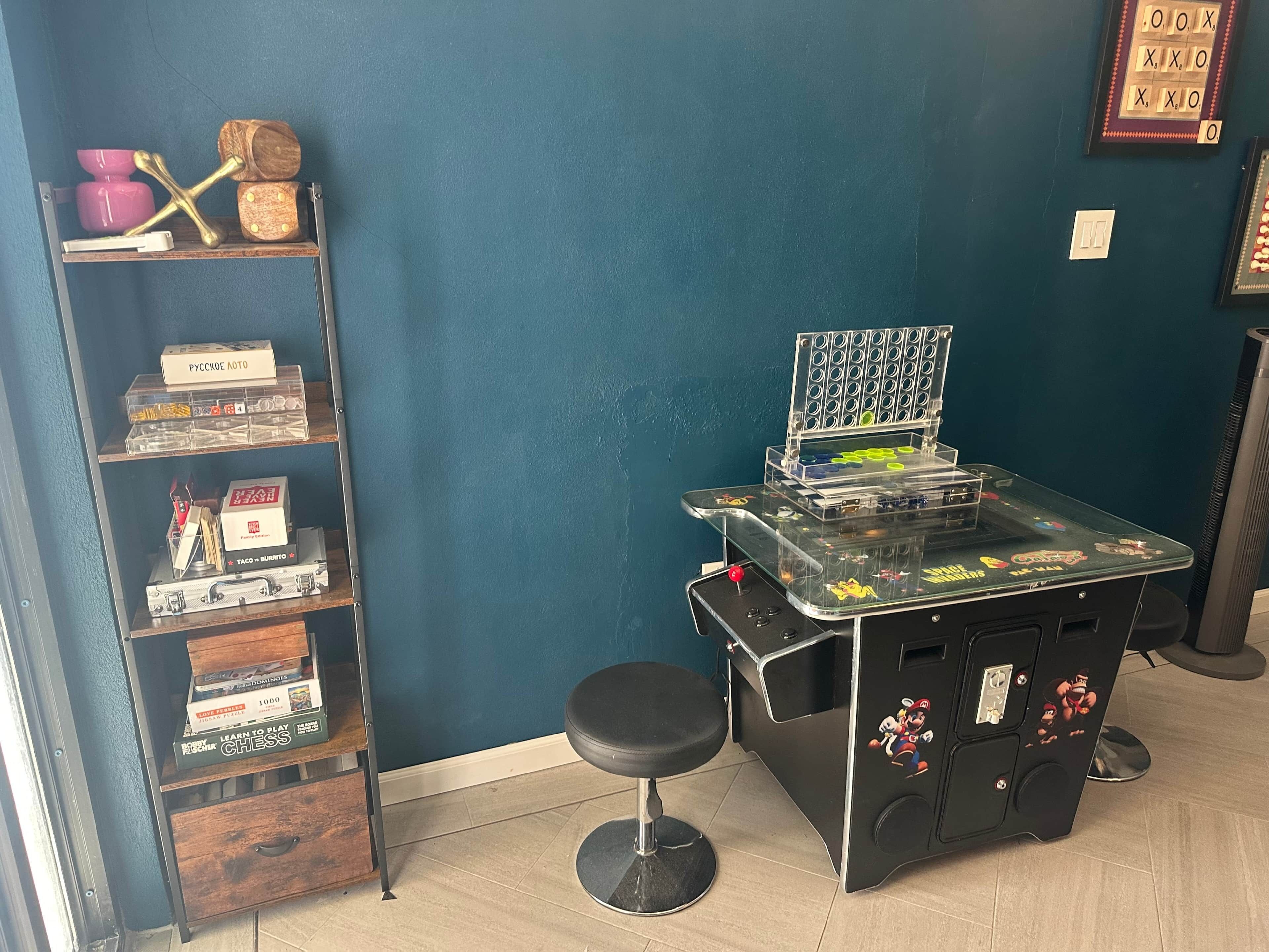 Ein Zimmer mit blauer Wand, einem Regal mit diversen Gegenständen, einem Tisch mit einem Schachspiel und einem Mario-Sessel.