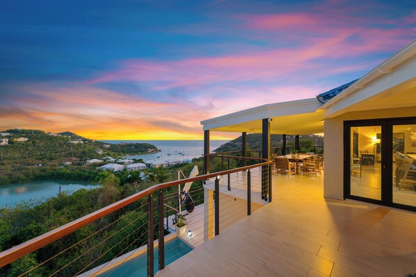 A modern balcony with a glass railing overlooking a scenic coastal view during sunset.