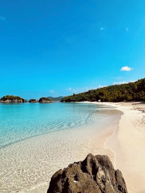 A beach with clear turquoise water, white sand, and rocky outcrops.
