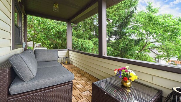 A covered porch with a wicker sofa, a glass table with flowers, and a view of trees. - Obies Abode: Newly Renovated (Pittsburgh)