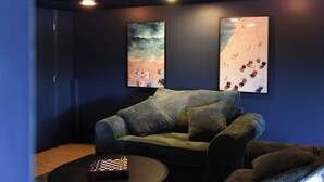 A room with a dark blue wall, a grey sofa, and two framed artworks depicting abstract beach scenes. - Obies Abode: Newly Renovated (Pittsburgh)