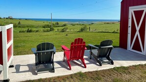 A red barn with a white door, three Adirondack chairs, and a view of the ocean. - Country cottage, exceptional view, lake, dunes and sea. 5 minutes from the beach (Kensington)