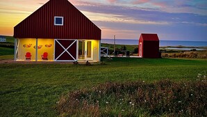 A red barn with a large open door and two red chairs outside, set against a sunset sky. - Country cottage, exceptional view, lake, dunes and sea. 5 minutes from the beach (Kensington)
