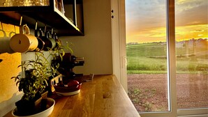 A kitchen with a wooden countertop, a potted plant, and a view of a sunset through a glass door. - Country cottage, exceptional view, lake, dunes and sea. 5 minutes from the beach (Kensington)