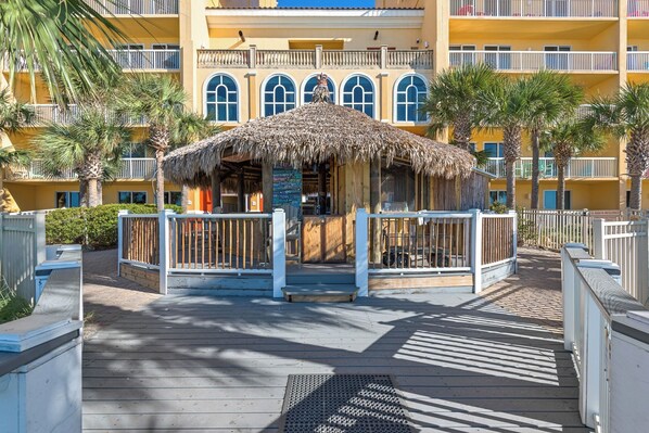 Un resort con una estructura de techo de paja, una terraza de madera y un edificio de varios pisos con balcones.
