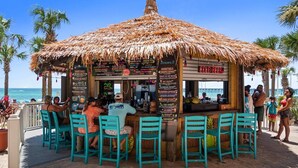 Un bar en la playa con techo de paja, mesas al aire libre y un cartel de menú.
