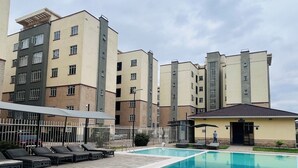 Une piscine dotée de chaises longues et d’une zone délimitée par une clôture, le tout entouré d’immeubles à plusieurs étages avec des balcons.