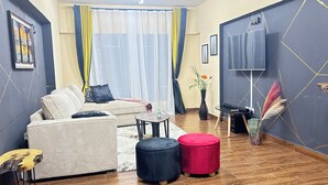 Un salon moderne avec un canapé, des poufs, une table basse et un téléviseur à écran plat.