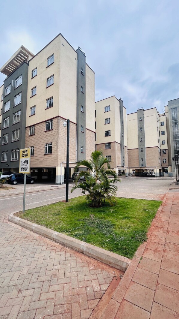 A multi-story residential building with a 'SLOW DOWN CHILDREN PLAYING' sign, a small palm tree, and a paved walkway.