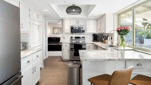 A modern kitchen with white cabinetry, a central island, and a large window providing a view of the outdoors.