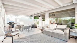 An outdoor patio area with wicker furniture, a grill, and a large window offering a view of the outdoors.