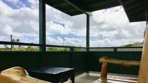 Terraza de madera con un banco y una pequeña mesa, con vistas a un paisaje escénico con nubes y vegetación.