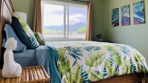 Un dormitorio con cama, ventilador de techo, ventana con cortinas y tres cuadros colgados en la pared.