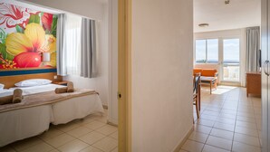 A hotel room with a bed, a painting of flowers on the wall, a balcony with a view, and a dining area.