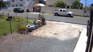 A residential street with a white pickup truck parked on the side, a gravel driveway, and a small garden area with tires and plants. - Rincon Sunset Studio (Rincon)