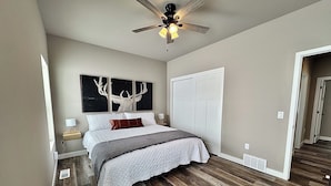 A bedroom with a bed, a ceiling fan, a nightstand, a lamp, and a wall with three framed pictures.