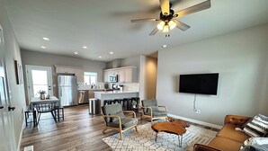 A spacious living area with a dining table, chairs, a sofa, and a TV mounted on the wall.