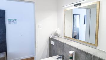 A modern bathroom with a white sink, a large mirror, and a towel dispenser.