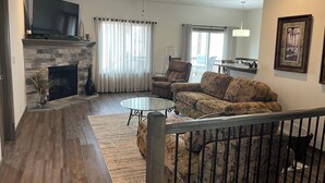 A living room with a stone fireplace, a ceiling fan, a sofa, a coffee table, and a staircase. - Spacious 4-bedroom house with AC, WiFi in NW Lincoln (Lincoln)