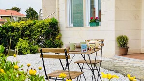 Une terrasse avec une table et des chaises en bois, entourée de petits galets blancs et de fleurs jaunes.