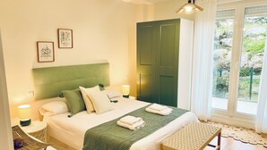 Une chambre à coucher bien aménagée, avec un lit, des lampes de chevet, un banc et une vue sur l’extérieur.