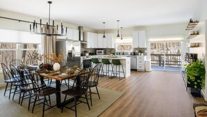 A modern kitchen with white cabinets, a central island, and a dining area with dark chairs.
