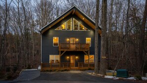 A two-story log cabin with a balcony, large windows, and a front porch.