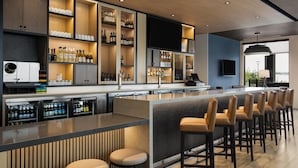 A modern bar area with a long counter, multiple shelves of bottles, and a seating area with stools. - Hyatt Place Billings (Billings)