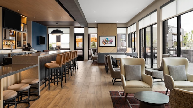 A modern bar area with a long counter, bar stools, and a seating area with tables and chairs. - Hyatt Place Billings (Billings)