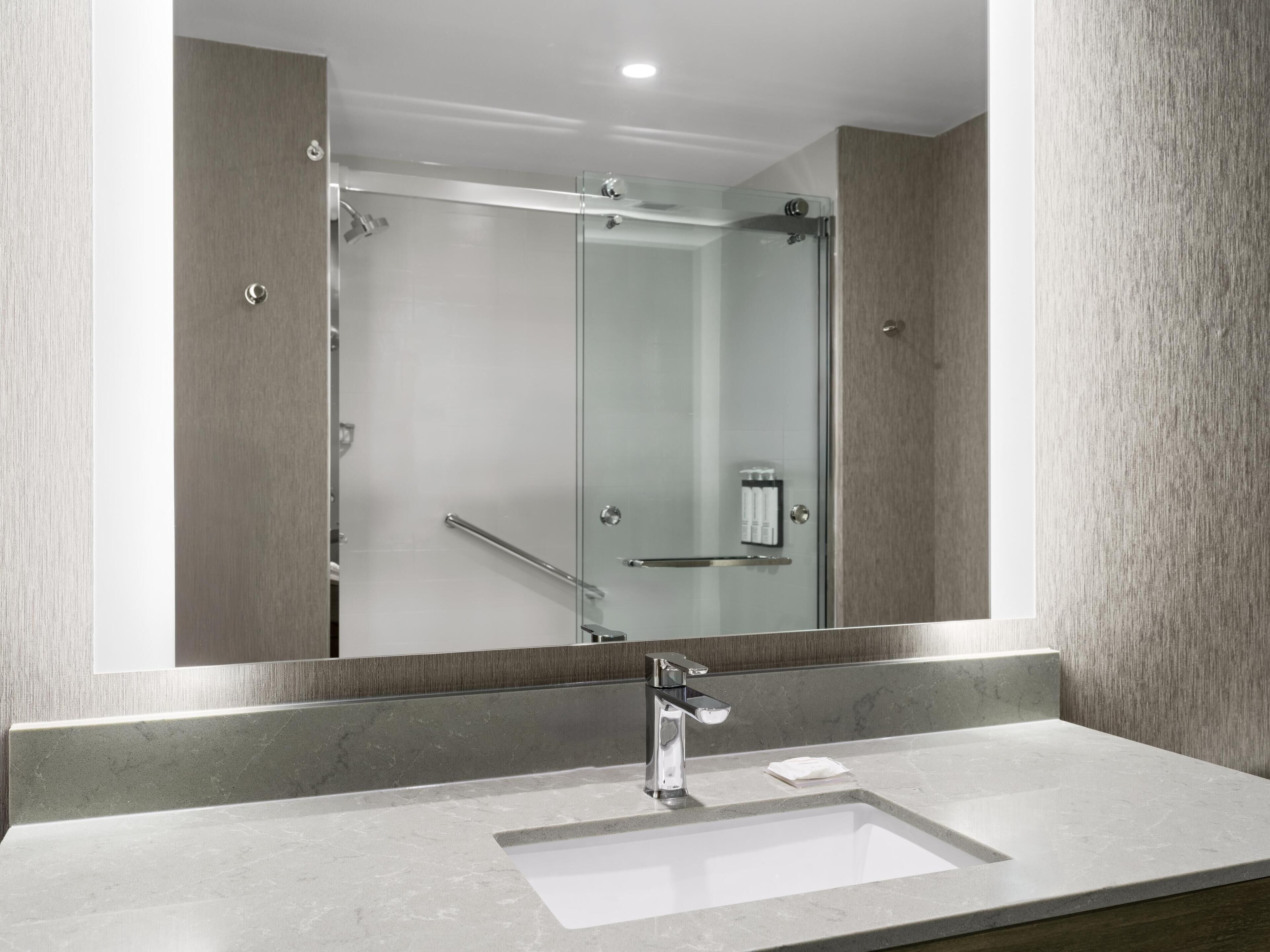 Een moderne badkamer met een douchecabine van glas, een chromen wastafel en een handdoekdispenser.