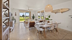 A spacious dining area with a white table set for four, surrounded by white chairs. A ceiling fan and a woven light fixture are visible.