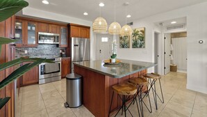 A modern kitchen with wooden cabinets, stainless steel appliances, a granite countertop, and a central island with bar stools.