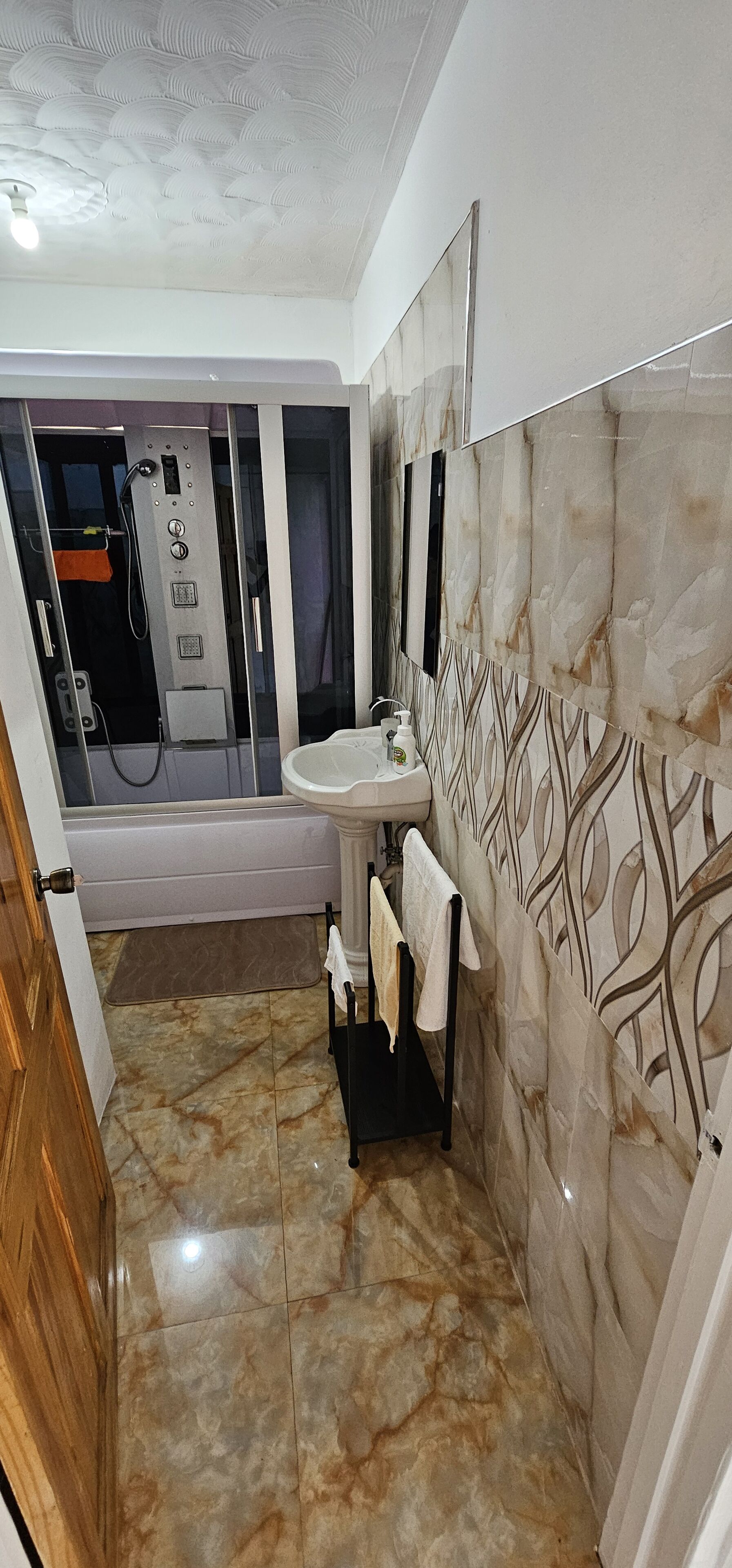 A bathroom with a marble floor, a sink, a towel rack, and a shower enclosure.