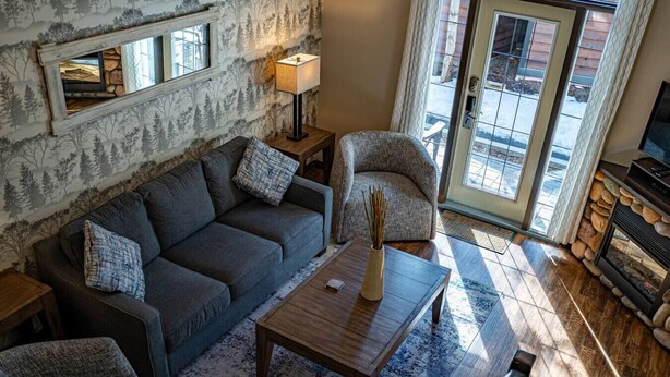 A cozy living room with a sofa, armchair, coffee table, and fireplace. - 2 Bedroom at Mystic Springs Chalets & Hot Pools (Canmore)